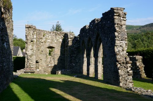 The remains of Cymer Abbey; stone walls with arches.