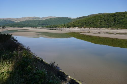A wide river with sand banks, tree-covered hills in the background.