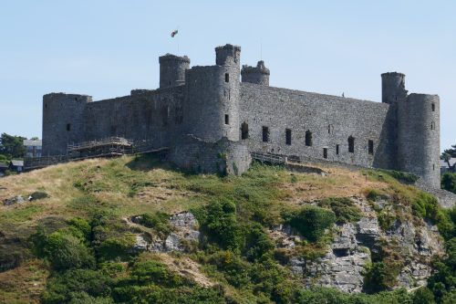 A castle on top of a rocky outcrop. A round tower is in each corner, with taller towers in the background.