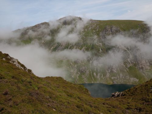 Grassy mountain landscape with clouds sinking between the peaks.