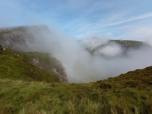 Grassy mountain landscape with clouds sinking between the peaks.